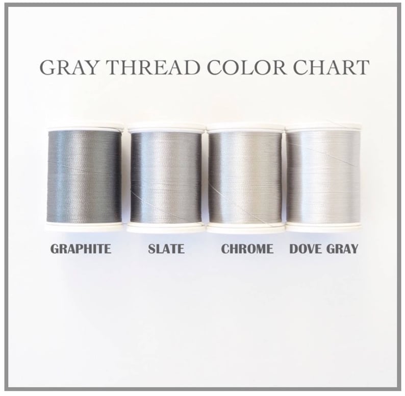 Op de afbeelding: Een kleurenkaart met vier spoelen grijze draad: Grafiet, Leisteen, Chroom en Duifgrijs. De tekst "GRAY THREAD COLOR CHART" staat bovenaan. De spoelen staan op een witte achtergrond.