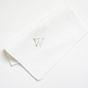 May include: White linen napkin with a silver embroidered letter W.