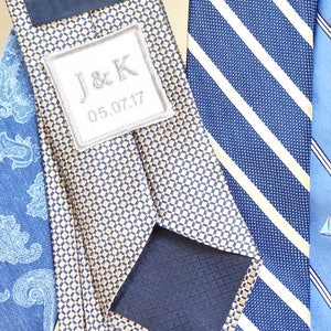 Peut inclure: Trois cravates à motifs différents. L'une est un motif géométrique or et bleu marine avec une étiquette blanche qui dit "J&K 05.07.17". Une autre est un motif rayé bleu marine et blanc. La troisième est un motif cachemire bleu marine.