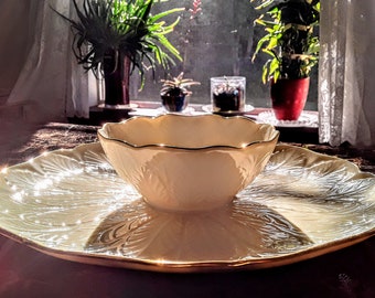 Könnte beinhalten: Eine weiße Porzellanservierschale mit goldfarbenem Rand und einer passenden Schüssel. Die Schale hat einen gewellten Rand und ein Blumenmuster. Die Schüssel steht auf der Schale.