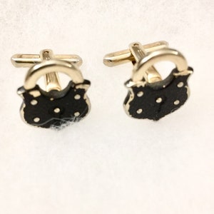 May include: A pair of gold-tone cufflinks shaped like padlocks. Each cufflink features a polished gold-tone metal loop at the top and a black, shield-shaped base with small, raised gold-tone dots arranged in a pattern across the front surface.