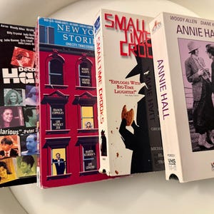 Pode incluir: Quatro fitas VHS com os filmes intitulados Deconstructing Harry, New York Stories, Small Time Crooks e Annie Hall. As capas exibem vários designs gráficos, incluindo uma ilustração de um edifício vermelho, uma silhueta e fotografias a preto e branco.