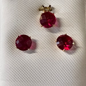 May include: A set of 14KT gold jewelry featuring a pendant and earrings with red gemstones.