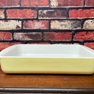May include: A white rectangular baking dish with a light yellow rim. The dish is made of ceramic and has a smooth, glossy finish.