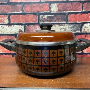 May include: A brown and black enamel pot with a black lid and black handles. The pot has a geometric pattern of brown squares with black clover symbols.