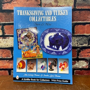 May include: A blue book titled "THANKSGIVING AND TURKEY COLLECTIBLES Then & Now" featuring images of turkey-themed collectibles. The cover includes a decorative plate, a vintage postcard, and various turkey figurines. The book is a Schiffer Book for Collectors.