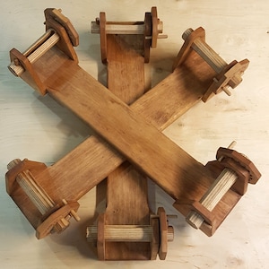 Puede incluir: Un ovillador de hilo de madera, una herramienta para enrollar el hilo en una madeja. El ovillador es de madera marrón clara y oscura, con un diseño en forma de estrella. Tiene varios componentes de madera.