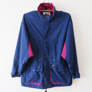 Könnte beinhalten: Eine blaue Vintage-Jacke mit magentafarbenen Akzenten. Die Jacke hat einen hohen Kragen, Druckknöpfe und zwei Vordertaschen. Der Innenkragen und die Seitenteile sind magenta. Die Jacke hängt an einem Holzkleiderbügel.