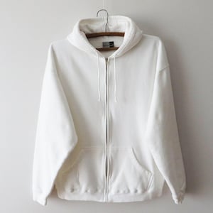 Könnte beinhalten: Ein weißer Kapuzenpullover mit Reißverschluss, Kordelzugkapuze und Vordertaschen. Der Sweatshirt hängt an einem Holzkleiderbügel vor einem schlichten weißen Hintergrund. Der Hoodie besteht aus einem weichen, bequemen Material.