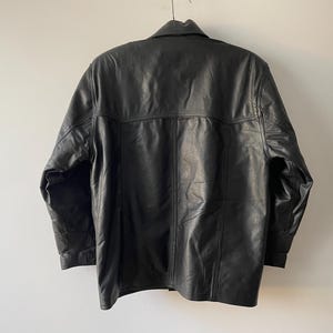 Pu&ograve; includere: Giacca in pelle nera con collo e polsini abbottonati. La giacca ha un design classico con chiusura a bottoni e una vestibilit&agrave; su misura. La parte posteriore della giacca &egrave; visibile, mostrando le cuciture e la consistenza della pelle.