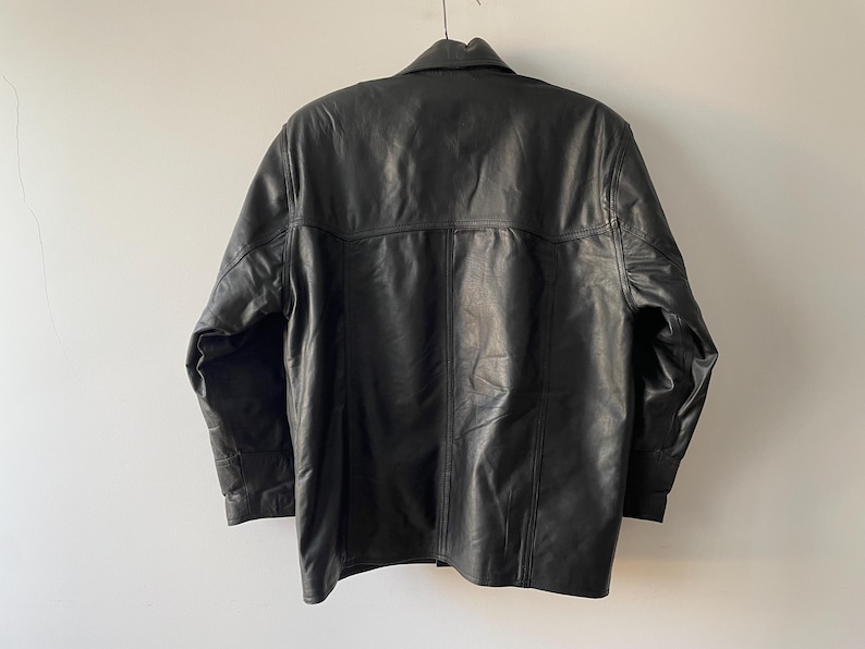 Pu&ograve; includere: Giacca in pelle nera con collo e polsini abbottonati. La giacca ha un design classico con chiusura a bottoni e una vestibilit&agrave; su misura. La parte posteriore della giacca &egrave; visibile, mostrando le cuciture e la consistenza della pelle.