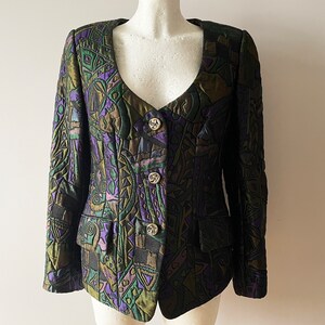 Peut inclure: Un blazer matelassé avec un motif géométrique unique dans les tons de vert, violet et noir. La veste présente un col cranté, trois boutons décoratifs et deux poches avant. Le blazer est présenté sur un mannequin.