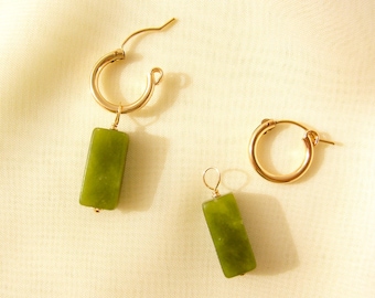 May include: A pair of gold hoop earrings with green stone dangles. The earrings are simple and elegant.