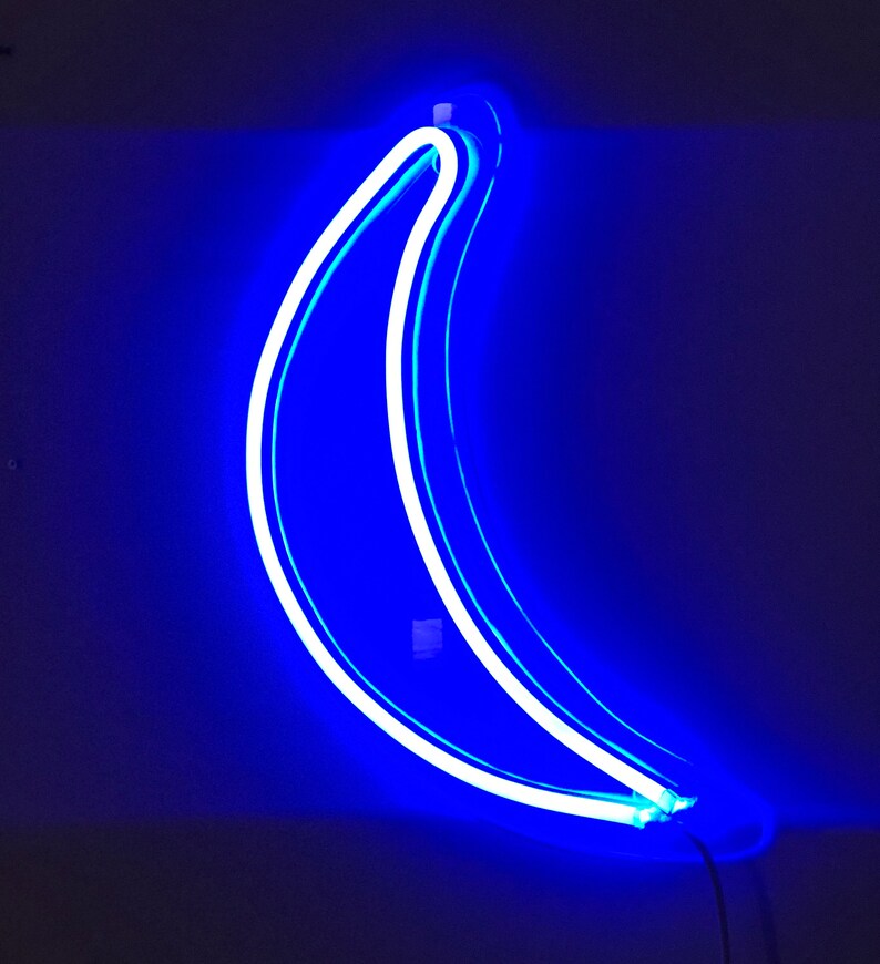 May include: A blue neon sign shaped like a banana. The sign is lit up and glowing against a dark background.