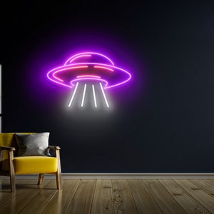 Puede incluir: Un letrero de ne&oacute;n con forma de platillo volante con luces rosas y moradas. El letrero est&aacute; montado en una pared oscura y est&aacute; iluminado con luz blanca.