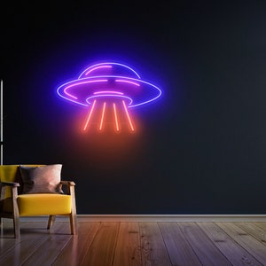 Puede incluir: Un letrero de ne&oacute;n con forma de platillo volante con un contorno morado y azul y rayos de luz rojos. El letrero est&aacute; montado en una pared oscura en una habitaci&oacute;n con un sill&oacute;n amarillo.