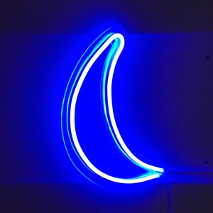 May include: A blue neon crescent moon sign. The neon light is white and the background is dark blue.