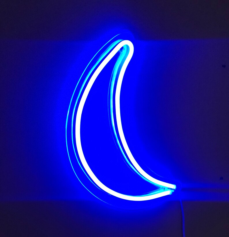 May include: A blue neon crescent moon sign. The neon light is white and the background is dark blue.