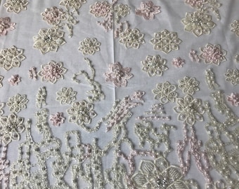Puede incluir: Tela blanca con un delicado patrón floral hecho de perlas y cuentas rosadas. La tela es transparente y tiene una textura suave y fluida.