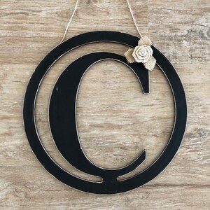 May include: Black wooden letter C wreath with a burlap and white fabric flower accent.