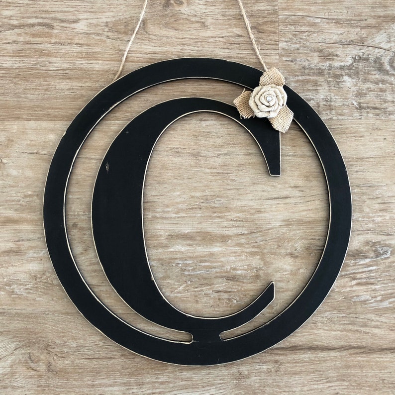 May include: Black wooden letter C wreath with a burlap and white fabric flower accent.