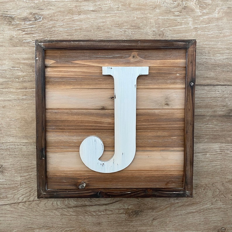 May include: A white wooden letter J in a rustic brown wood frame. The letter is distressed and has a whitewash finish.