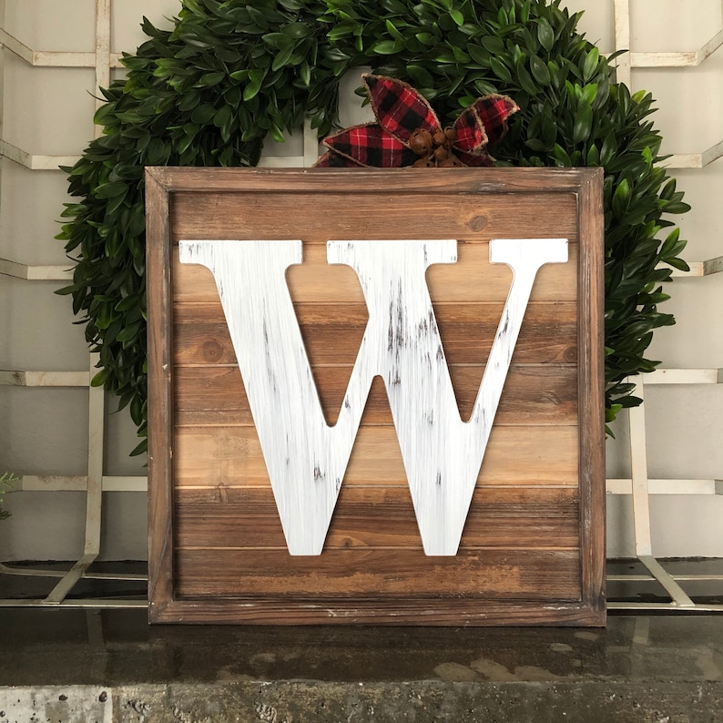 May include: A white wooden letter W in a rustic brown wood frame. The letter is distressed and has a whitewashed finish. The frame is made of reclaimed wood and has a natural finish.