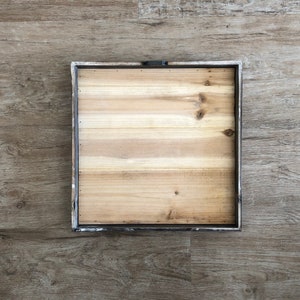 May include: A square wooden frame with a light brown wood surface. The frame has a distressed white paint finish and a metal hanging hook.