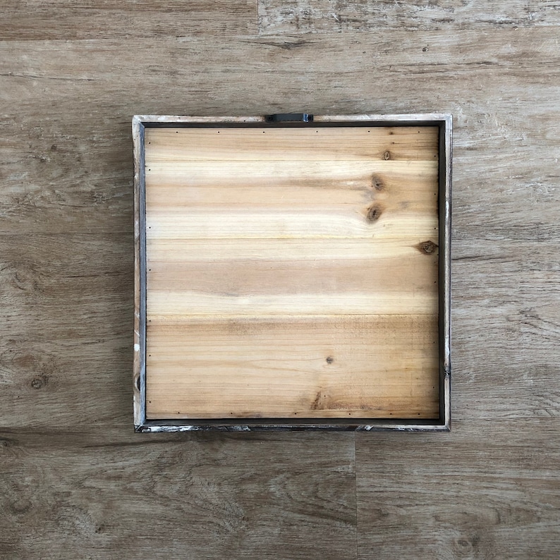 May include: A square wooden frame with a light brown wood surface. The frame has a distressed white paint finish and a metal hanging hook.