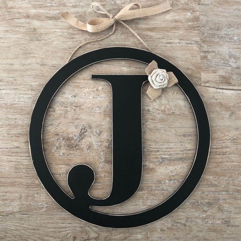 May include: Black wooden letter J with a white burlap flower, attached to a black circle with a burlap bow.