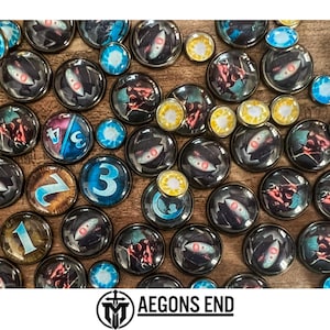 May include: A collection of colorful, round game tokens with various designs, including numbers, symbols, and abstract patterns. The tokens are made of glass and have a metallic finish. The tokens are arranged on a wooden surface. The text "AEGONS END" is visible at the bottom of the image.