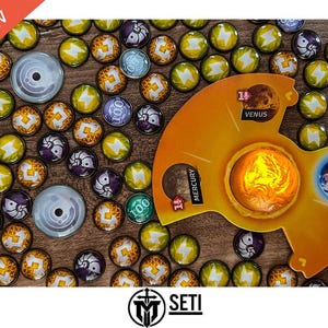 May include: A board game with a yellow, orange and white game board featuring the words "Mercury", "Venus" and "11". The game board is surrounded by small, colourful tokens with symbols and numbers on them. The game is called "SETI".
