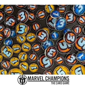 Puede incluir: Primer plano de una variedad de fichas redondas y coloridas con n&uacute;meros impresos en ellas. Las fichas est&aacute;n dispuestas en un patr&oacute;n aleatorio sobre una superficie oscura. El texto "MARVEL CHAMPIONS THE CARD GAME" est&aacute; impreso en la parte inferior de la imagen.