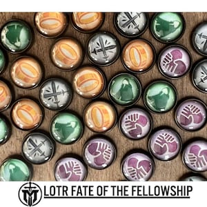 Può includere: Una collezione di pedine di gioco rotonde con vari disegni. Alcune presentano un anello d'oro, altre spade, figure in mantelli verdi o mani strette. I pezzi hanno un bordo metallico e sono disposti su una superficie di legno. Il testo "LOTR FATE OF THE FELLOWSHIP" è in basso.