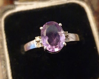 May include: A silver ring with a large oval amethyst gemstone and smaller accent stones.