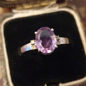 May include: A silver ring with a large oval amethyst gemstone and smaller accent stones.