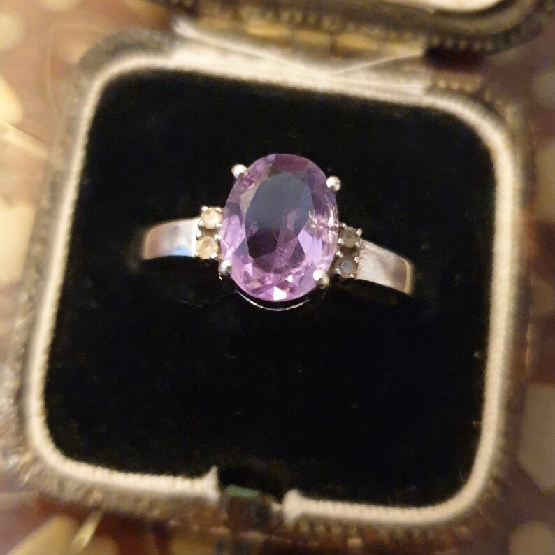 May include: A silver ring with a large oval amethyst gemstone and smaller accent stones.
