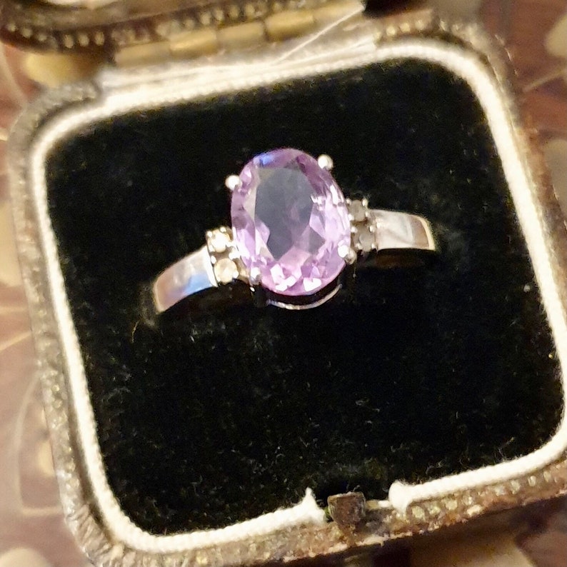 May include: A silver ring with a large oval amethyst gemstone and smaller diamond accents.