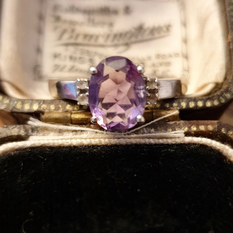 May include: A silver ring with a large oval amethyst gemstone and two smaller diamond accents.