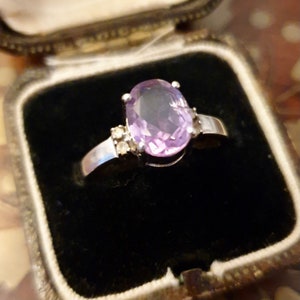 May include: A silver ring with a large oval amethyst gemstone and smaller clear gemstones on the band.
