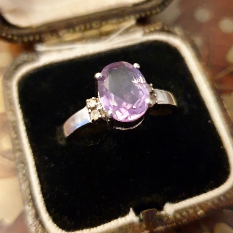 May include: A silver ring with a large oval amethyst gemstone and smaller clear gemstones on the band.