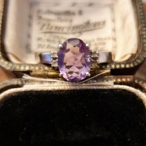 May include: A silver ring with a large oval amethyst gemstone and smaller diamond accents. The ring is in a velvet-lined jewelry box.