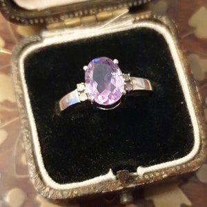 May include: A silver ring with a large oval-shaped amethyst gemstone surrounded by smaller clear gemstones.