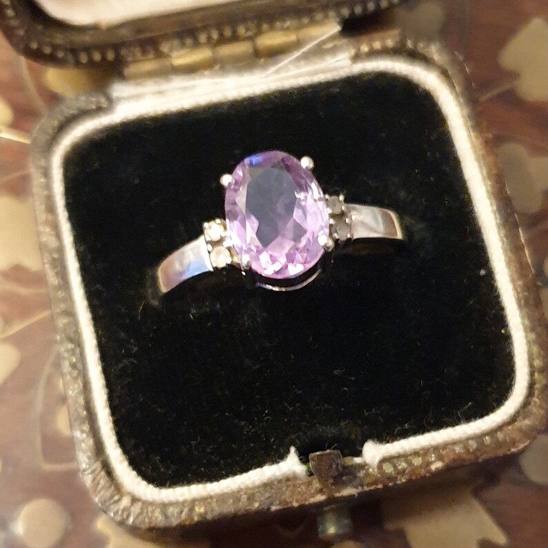 May include: A silver ring with a large oval-shaped amethyst gemstone surrounded by smaller clear gemstones.