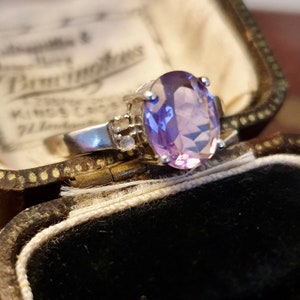 May include: A silver ring with a large oval amethyst gemstone and smaller clear gemstones on the band.