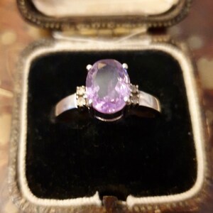 May include: A silver ring with a large oval-shaped amethyst gemstone and two smaller diamond accents.