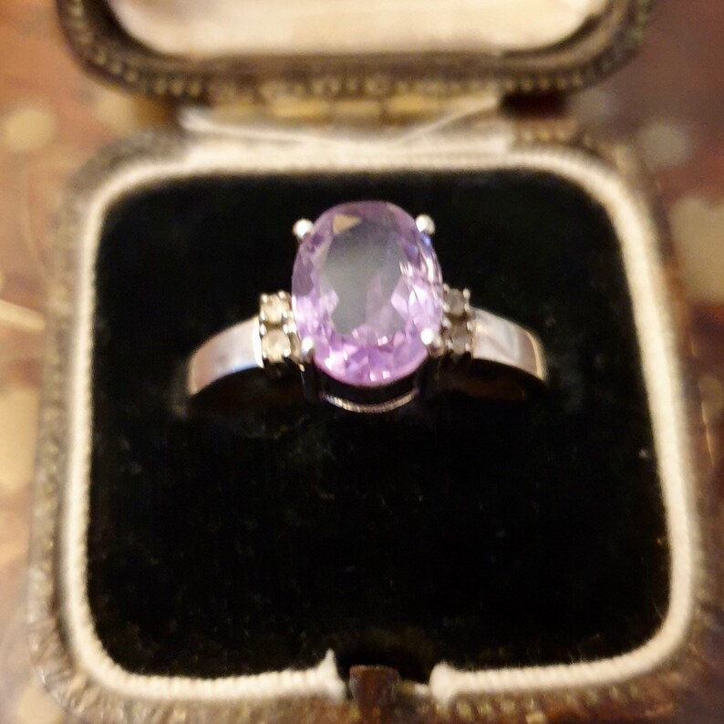 May include: A silver ring with a large oval-shaped amethyst gemstone and two smaller diamond accents.