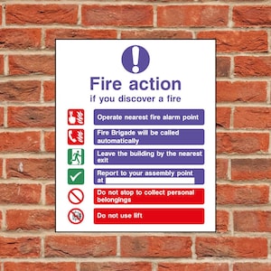 May include: A fire action sign with instructions in white text on a blue and red background. The sign is mounted on a red brick wall. The sign includes icons and text detailing fire safety procedures.