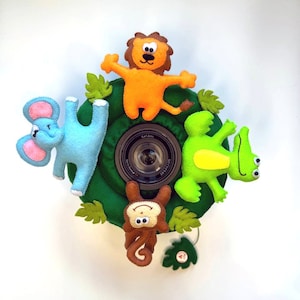 Könnte beinhalten: Ein grüner Filz-Objektivschutz mit einem Filz-Löwen, -Elefanten, -Affen und -Alligator. Der Objektivschutz ist mit grünen Filzblättern verziert.