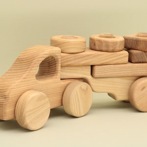 May include: A wooden toy truck with a flatbed and four wheels. The truck is carrying a stack of wooden blocks.